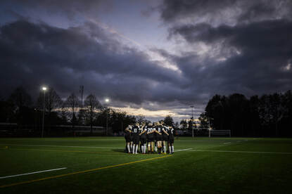 Een rugbyteam staat met de armen over elkaars schouders op een sporveld